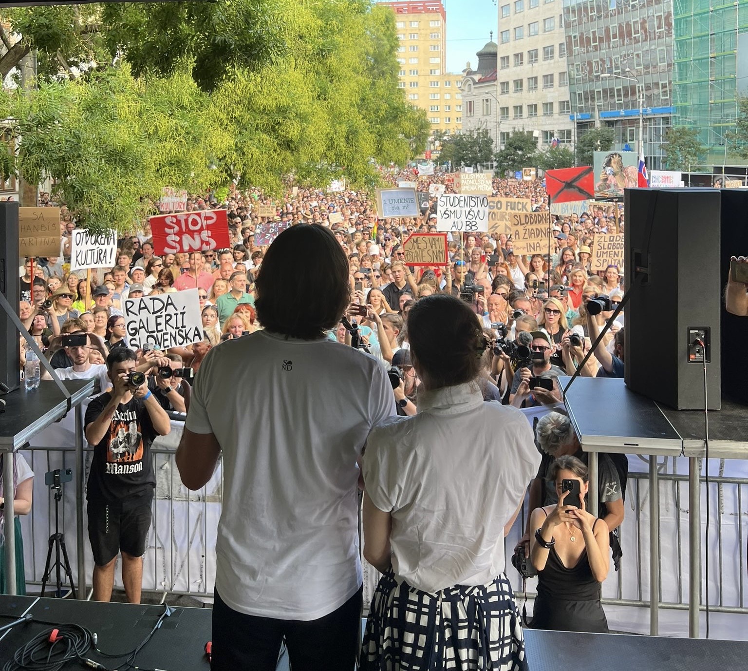 A man and a woman look at a crowd from a stage