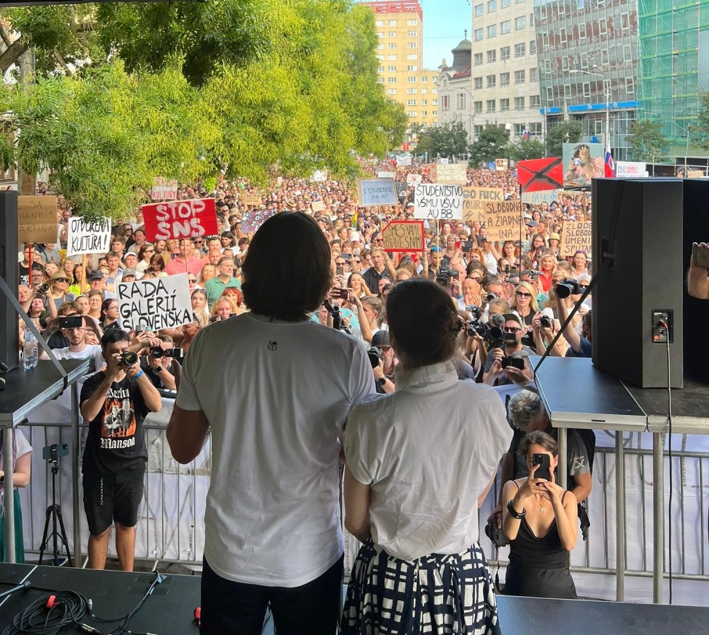 A man and a woman look at a crowd from a stage