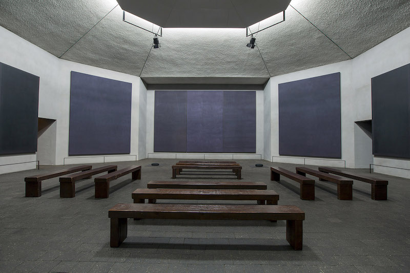 Five dark paintings in a chapel-like setting.