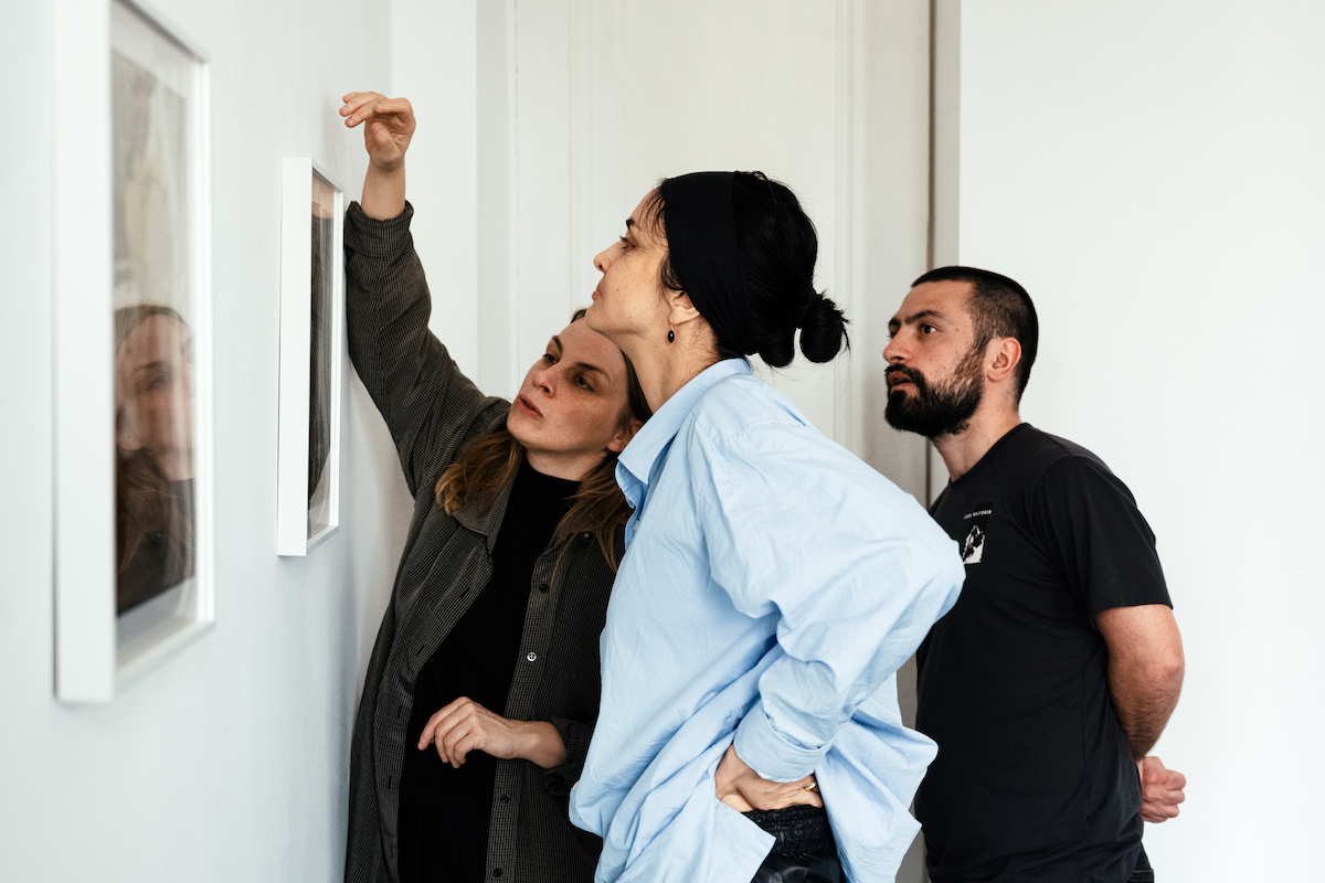 A woman looking at a framed photograph that is being hung by another woman. A man looks on behind them.