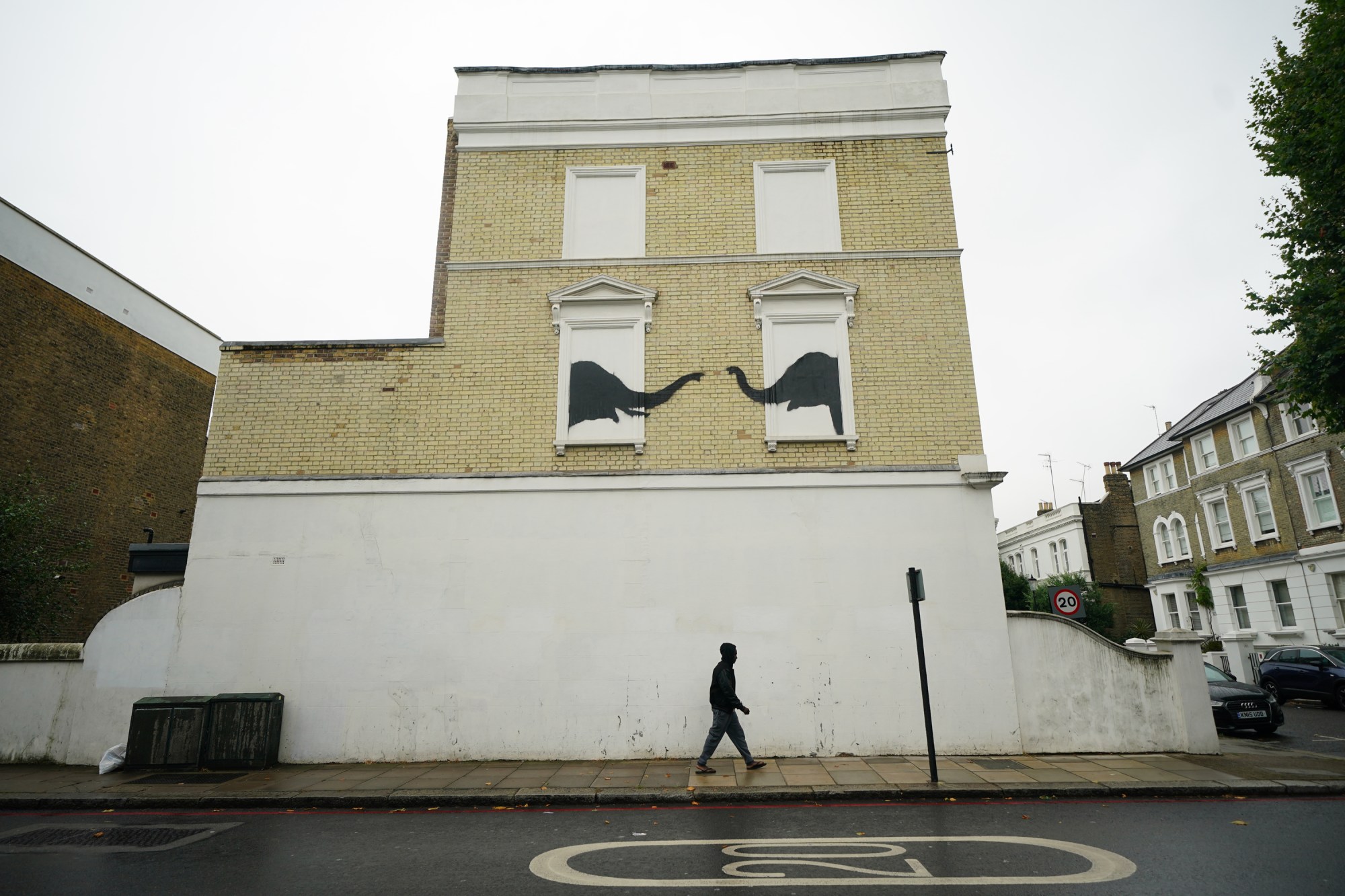 A man passes underneath a new artwork depicting two elephants poking their heads out of blocked out windows unveiled by Banksy on the side of a building at the junction of Edith Grove and Edith Terrace, in Chelsea, south west London. Picture date: Tuesday August 6, 2024. (Photo by Yui Mok/PA Images via Getty Images)