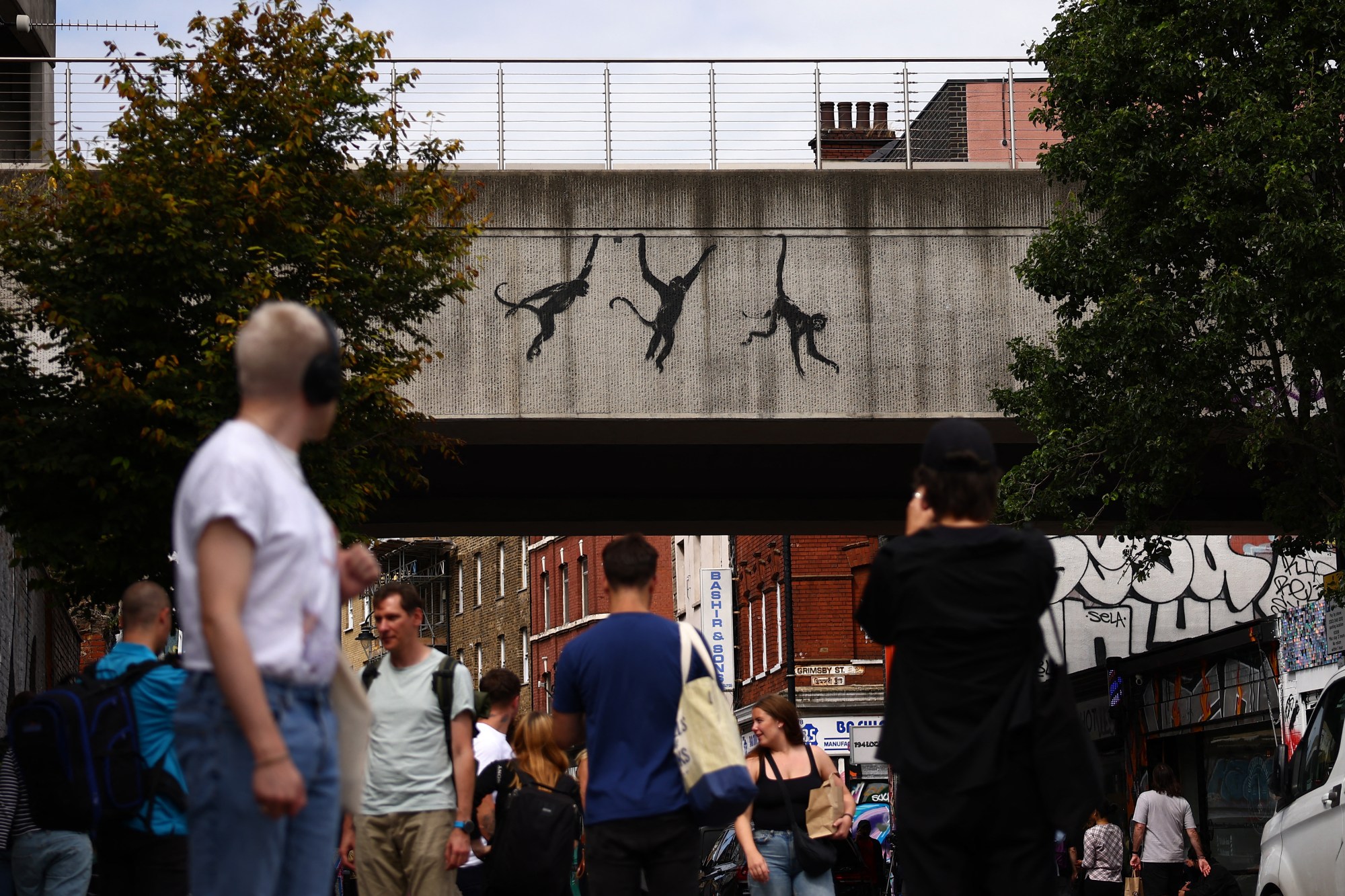 People walk past an artwork by street artist Banksy, the third to be released in three days, depicting three monkeys, painted on the side of a railway bridge in east London on August 7, 2024. The artist confirmed the work to be theirs after posting an image of it on the social media app Instagram. (Photo by HENRY NICHOLLS / AFP) / RESTRICTED TO EDITORIAL USE - MANDATORY MENTION OF THE ARTIST UPON PUBLICATION - TO ILLUSTRATE THE EVENT AS SPECIFIED IN THE CAPTION (Photo by HENRY NICHOLLS/AFP via Getty Images)