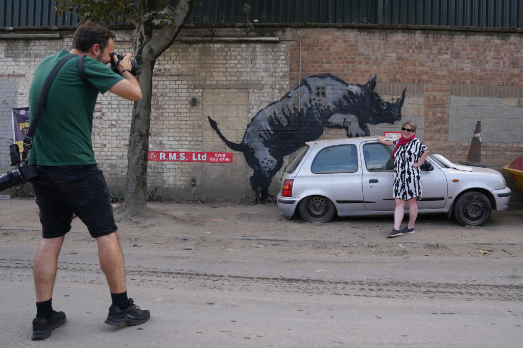 A woman poses for a photograph by a mural on a wall depicting a rhino