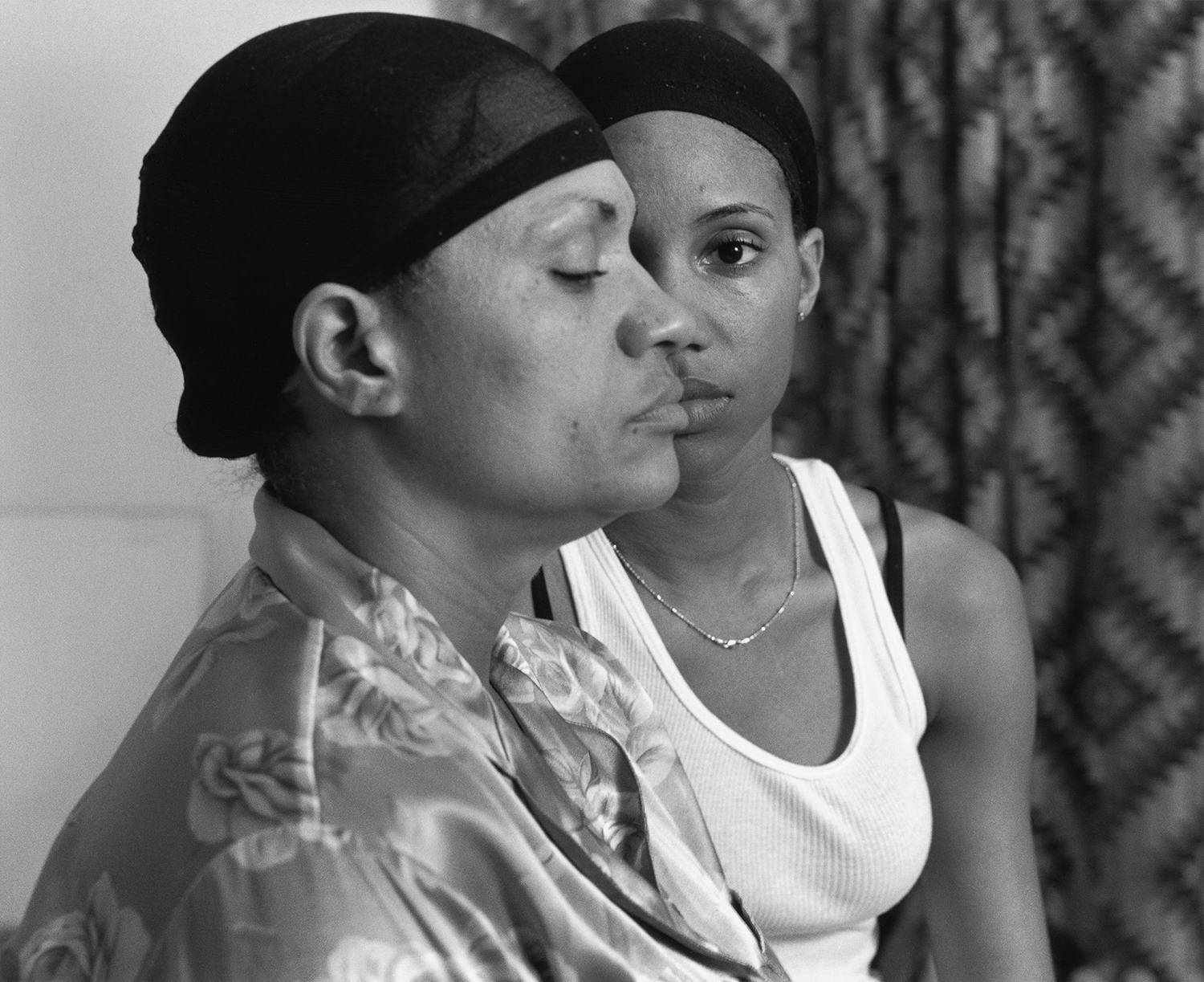 Two young black women are dressed casually, their faces eclipsing one another.