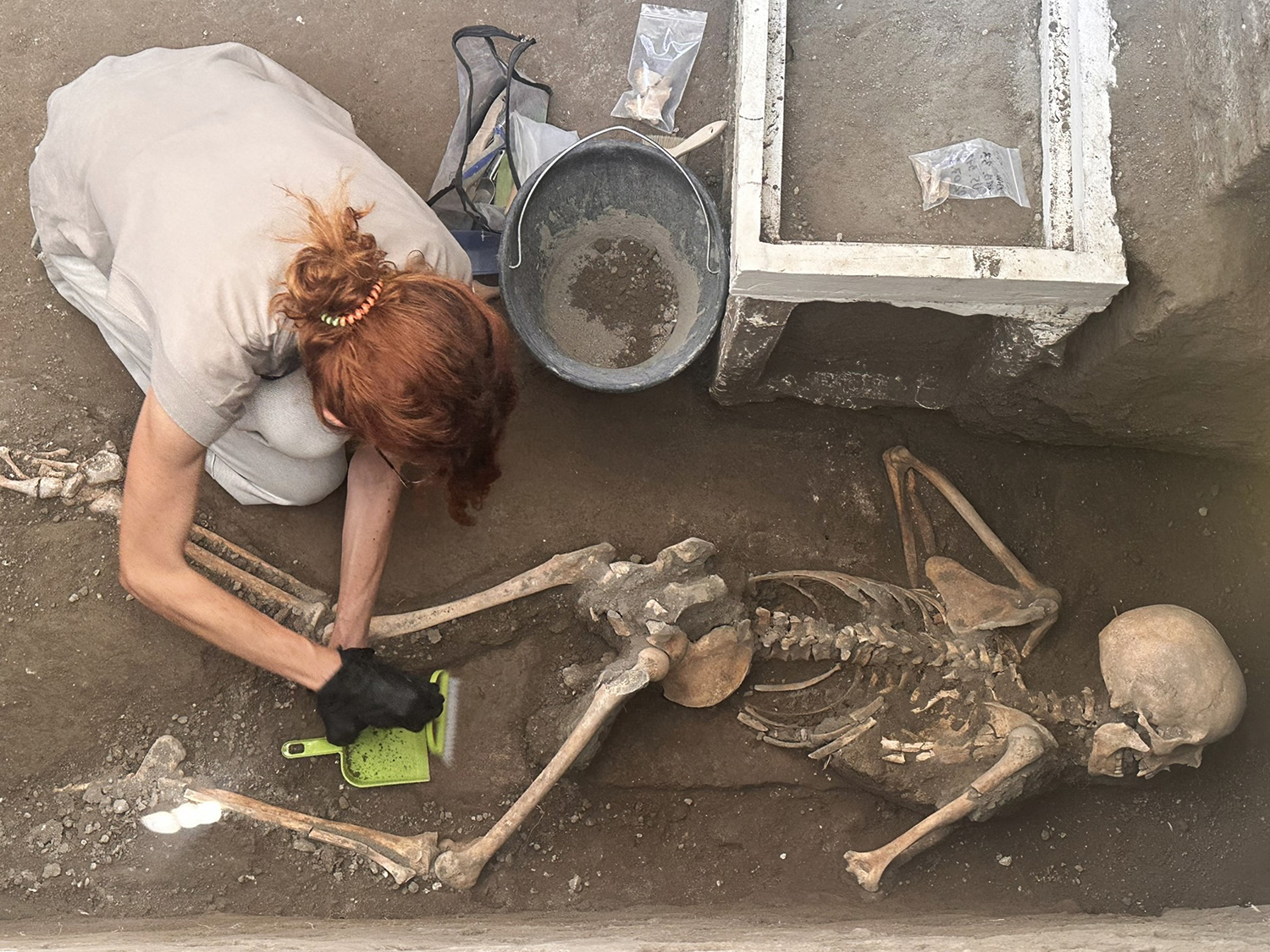 A female archaeologist carefully removes dust from a victim at Pompeii using a brush and dustpan.